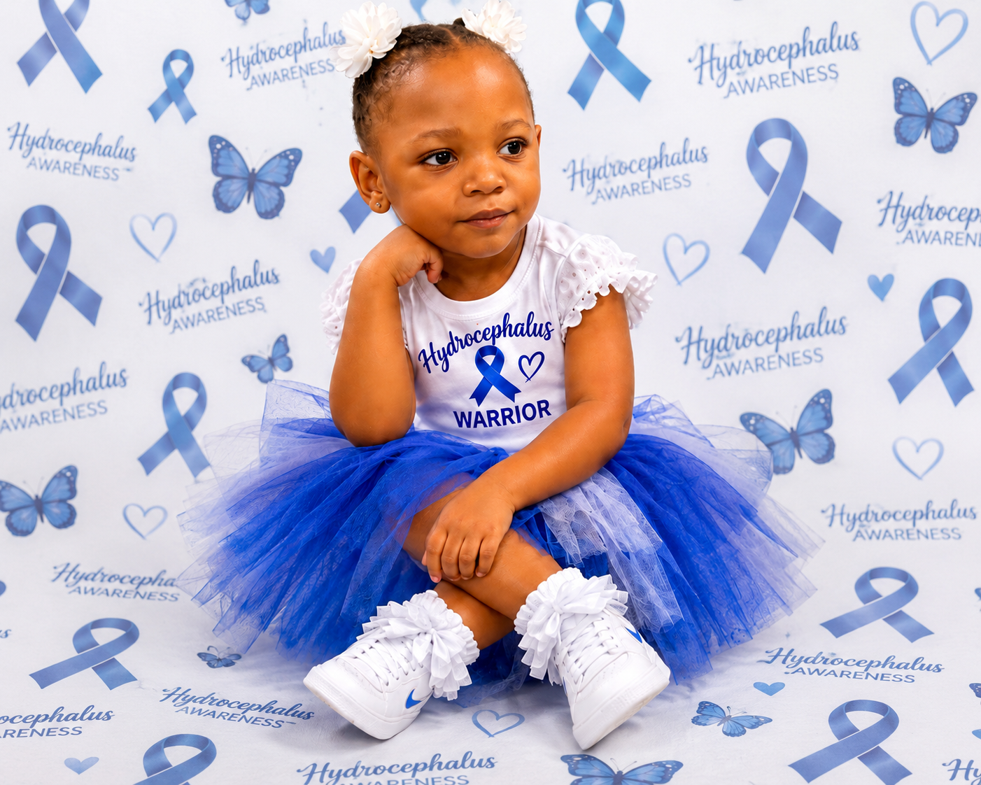 A young girl wearing a white Hydrocephalus Warrior awareness shirt with a blue ribbon, butterfly, and heart, paired with a blue tutu